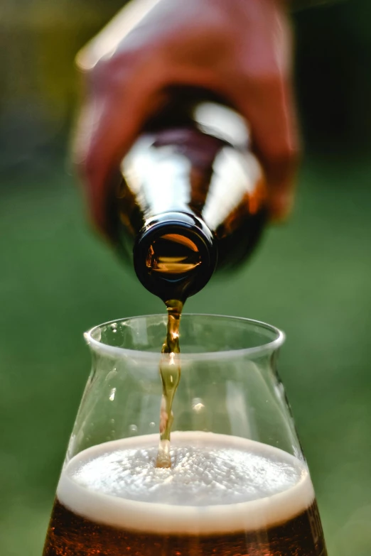 someone pouring beer in a large glass into another glass