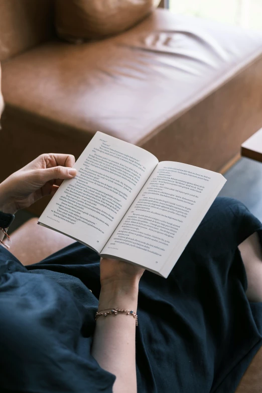 a person reading a book with her hands resting on a couch