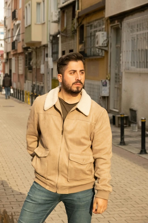 a man stands on a city street wearing a jacket and jeans