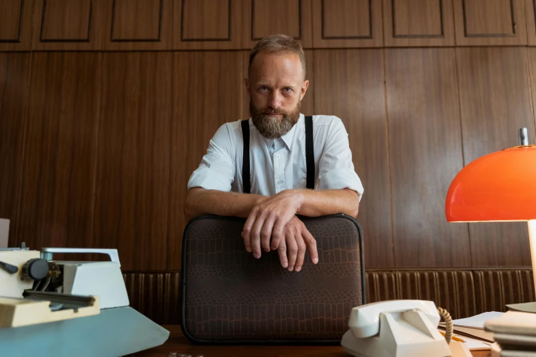 an older man leaning on his suitcase next to a desk