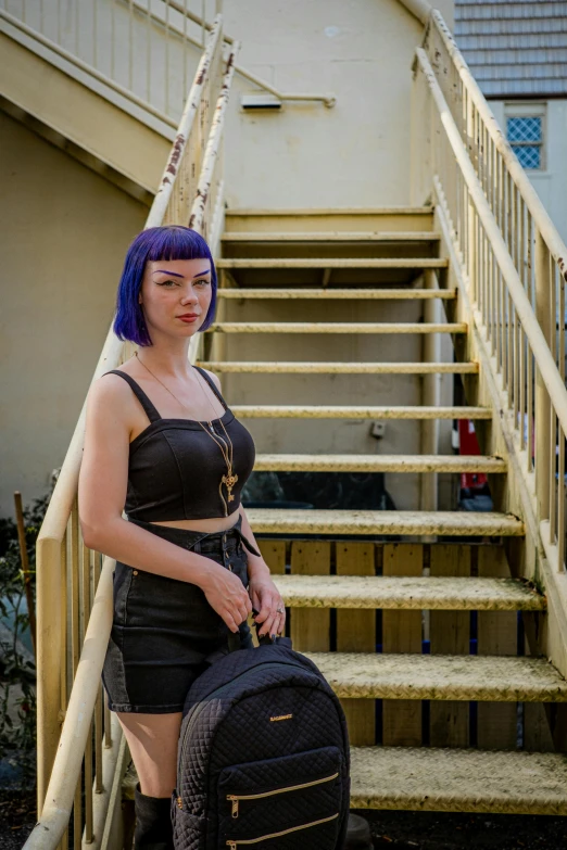 a girl with blue hair posing in front of stairs carrying a large backpack