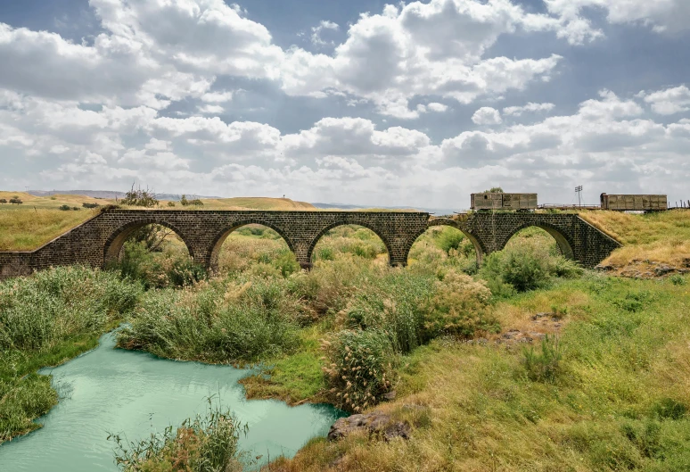 a bridge sits in a green field with a body of water