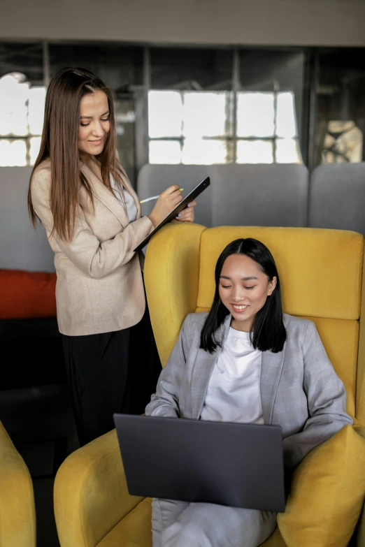 two women sitting in chairs looking at soing on a laptop