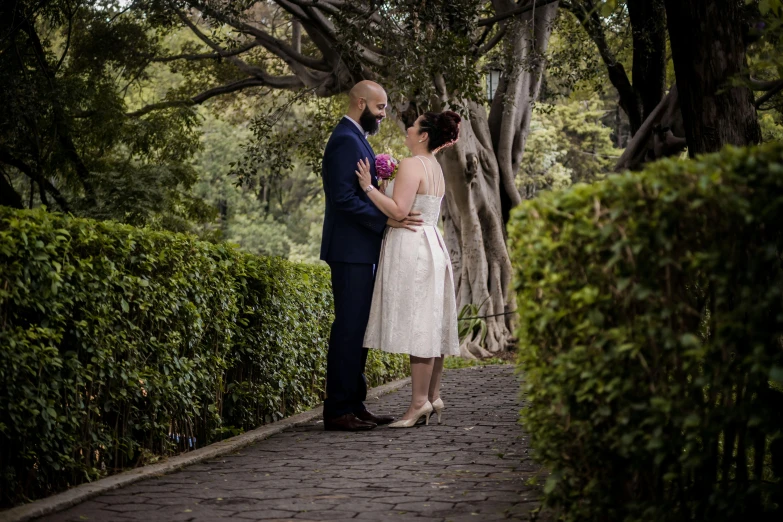 a newly married couple stand together on the cobblestone walkway in the woods