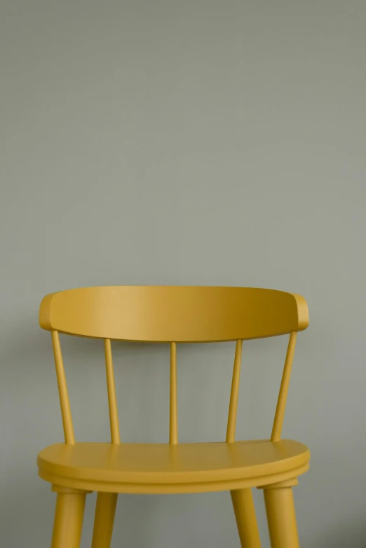 a yellow chair with a rounded seat against a gray wall