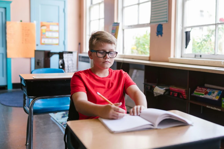 a boy sitting in a school desk writing