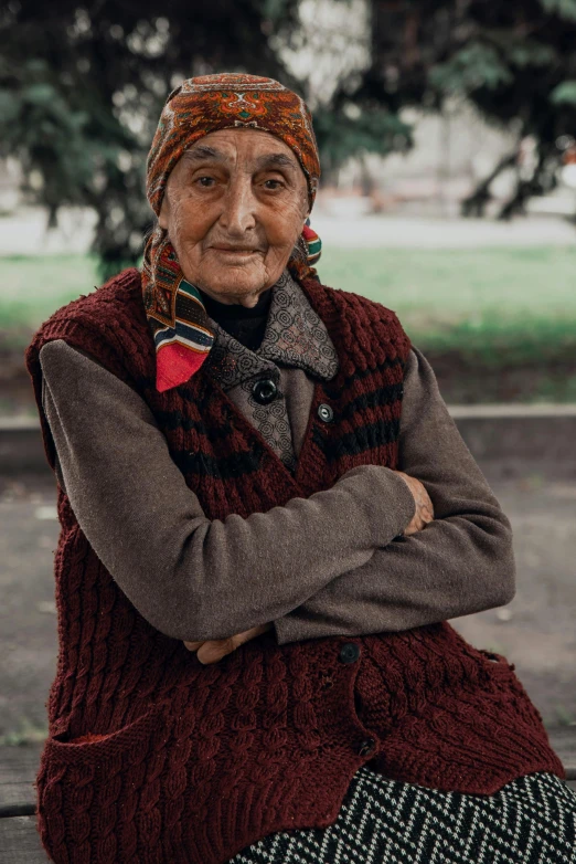 the old woman is sitting outside wearing a scarf