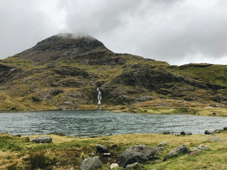 a small white building stands near a lake in front of a large mountain