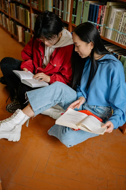 a man and woman sitting on the floor in front of a bookcase
