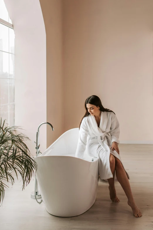 a woman in a bathrobe sits on a bench near a large tub