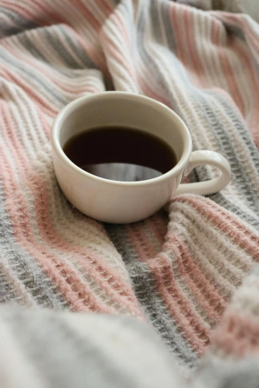 a white cup of coffee sitting on top of a blanket