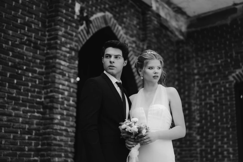 two people standing next to each other in front of a brick building