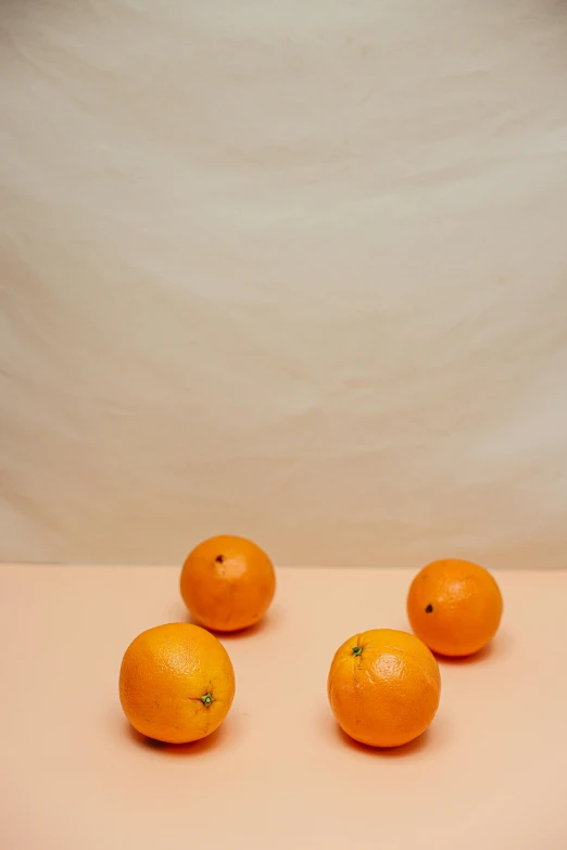 four oranges sit on a light colored table