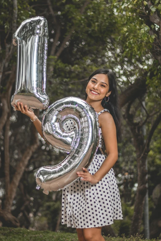 a woman holding up two large silver balloons