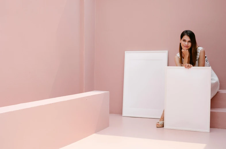 a woman sitting on a pink wall in front of white furniture