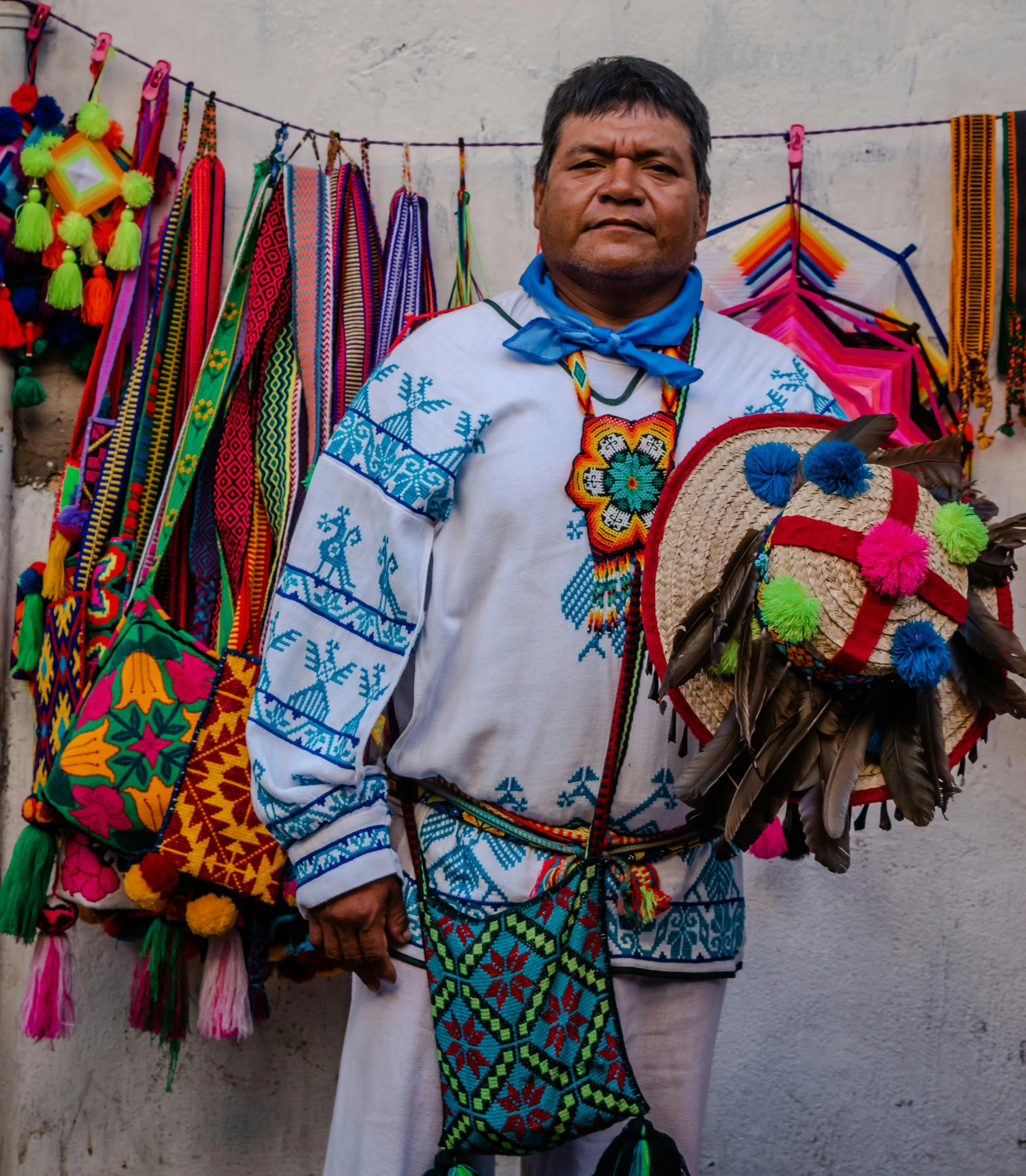 a man in white standing next to a wall with a collection of colorful accessories on it