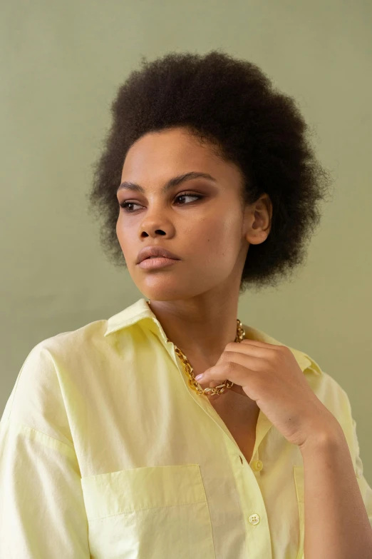 a woman poses wearing a yellow blouse with a golden necklace