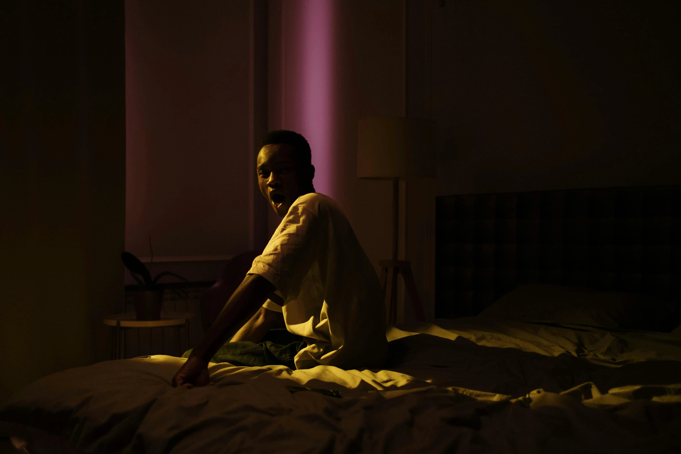 a man sits on a bed with no sheets in the dark