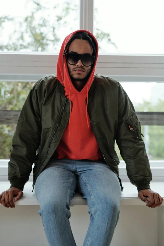 a man in sunglasses and hoodie sitting on a ledge