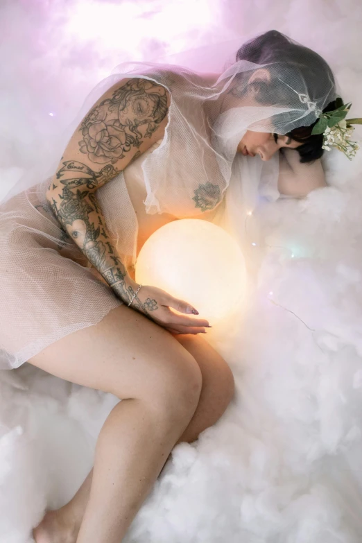 a tattooed woman in a dress sitting on cloud with ball