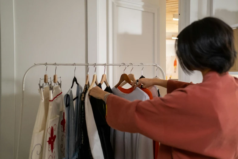 a woman reaching for clothing hanging on the clothes rack