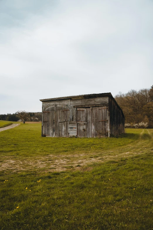 an old outhouse on a green field with trees