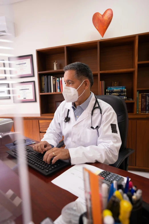 a doctor wearing a face mask sitting in a chair at his desk