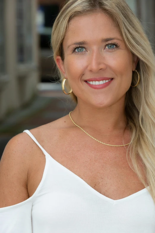 a blonde woman smiling and wearing gold jewelry