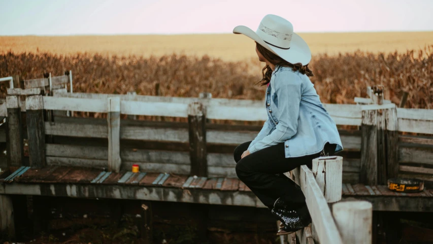 a woman in a hat is on a fence