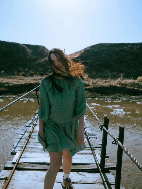 a woman in green dress crossing a long wooden bridge