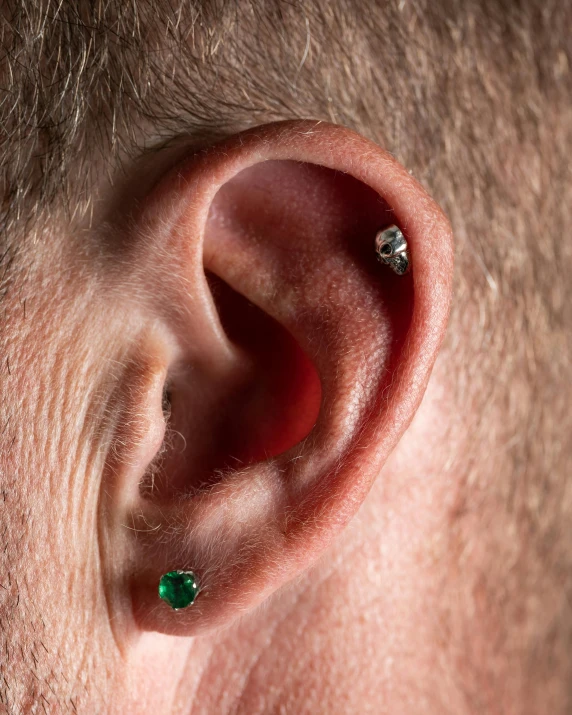 a man's ear with his nose ring and a pair of green stones
