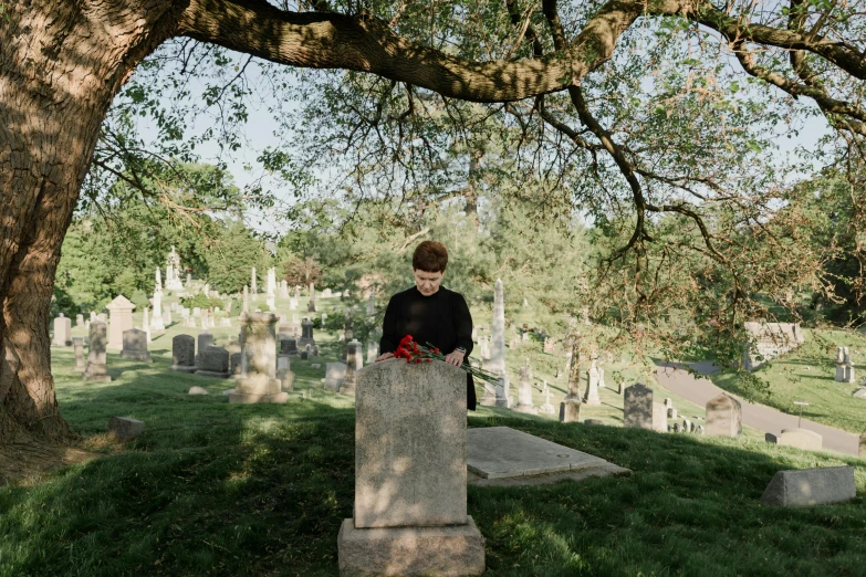 a person sitting on a grave under a large tree