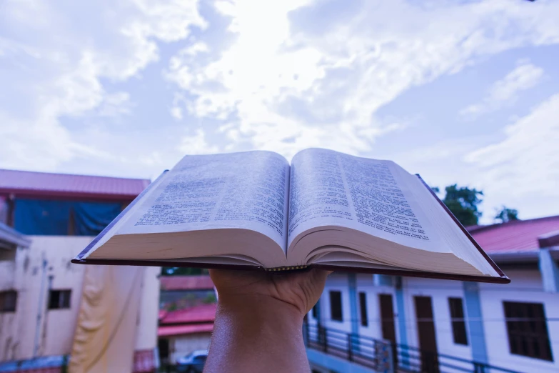 a person holding an open book over their head in the air