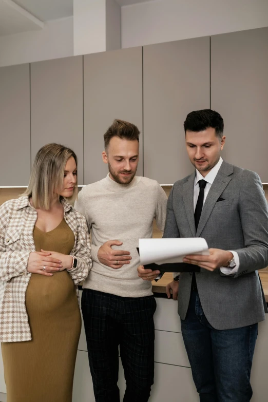 a man is standing with two woman in a kitchen looking at paperwork