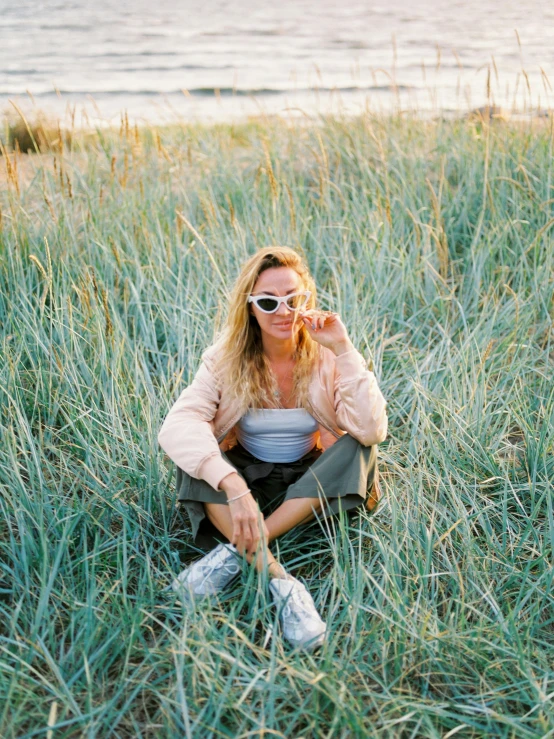 a girl sitting on the grass in sunglasses and smoking