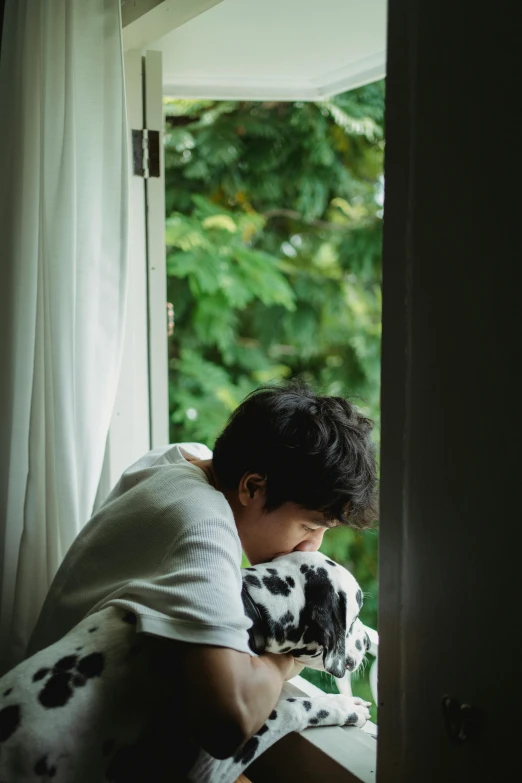 a boy in white shirt with dalmation bear on arm looking out window