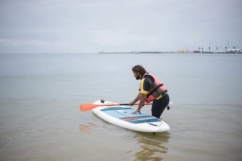 a man in the ocean holds an orange and blue surfboard