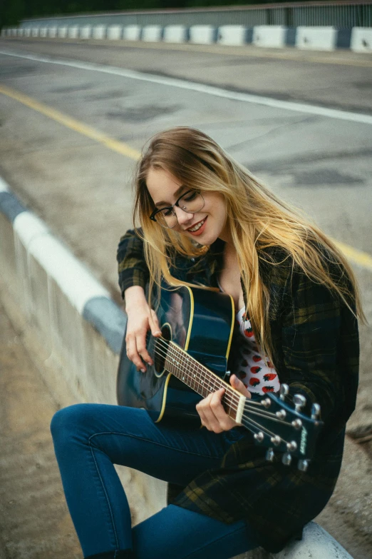 a woman with glasses, and a guitar is posing on a bridge