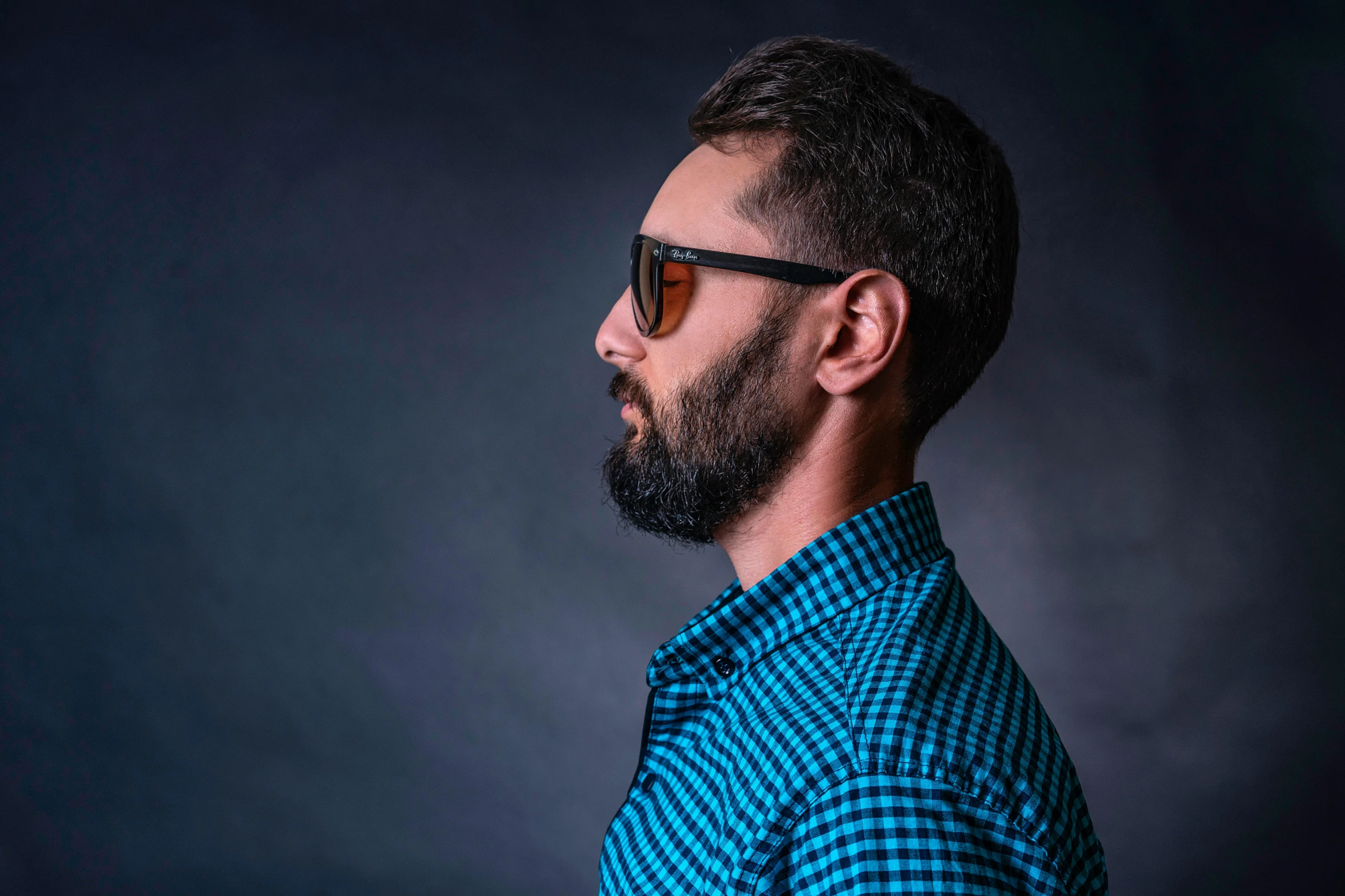 man with goatee and sunglasses looking to side, half of which is slightly undercut