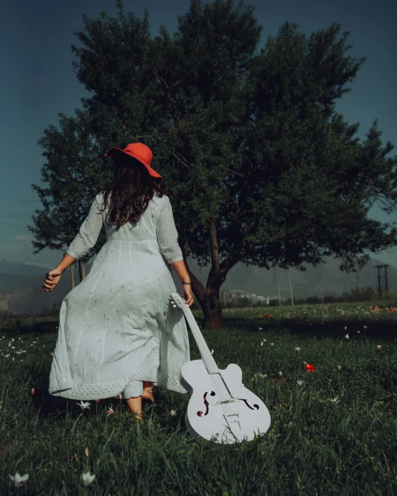 a woman walking with a guitar in the grass