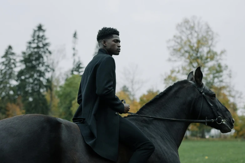 a man in a long black coat is on top of a black horse