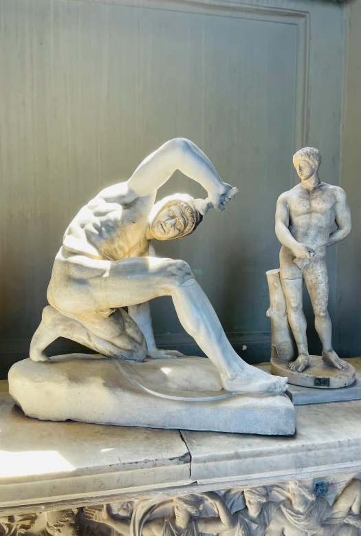 a statue of two men in various poses, one kneeling down while one stands up