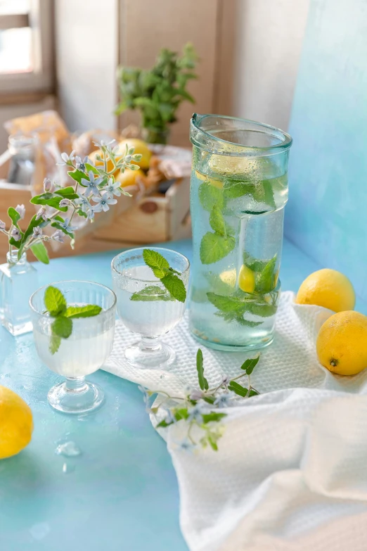 a glass vase with lemons and mints is sitting on a table next to a cup with lemon water in it