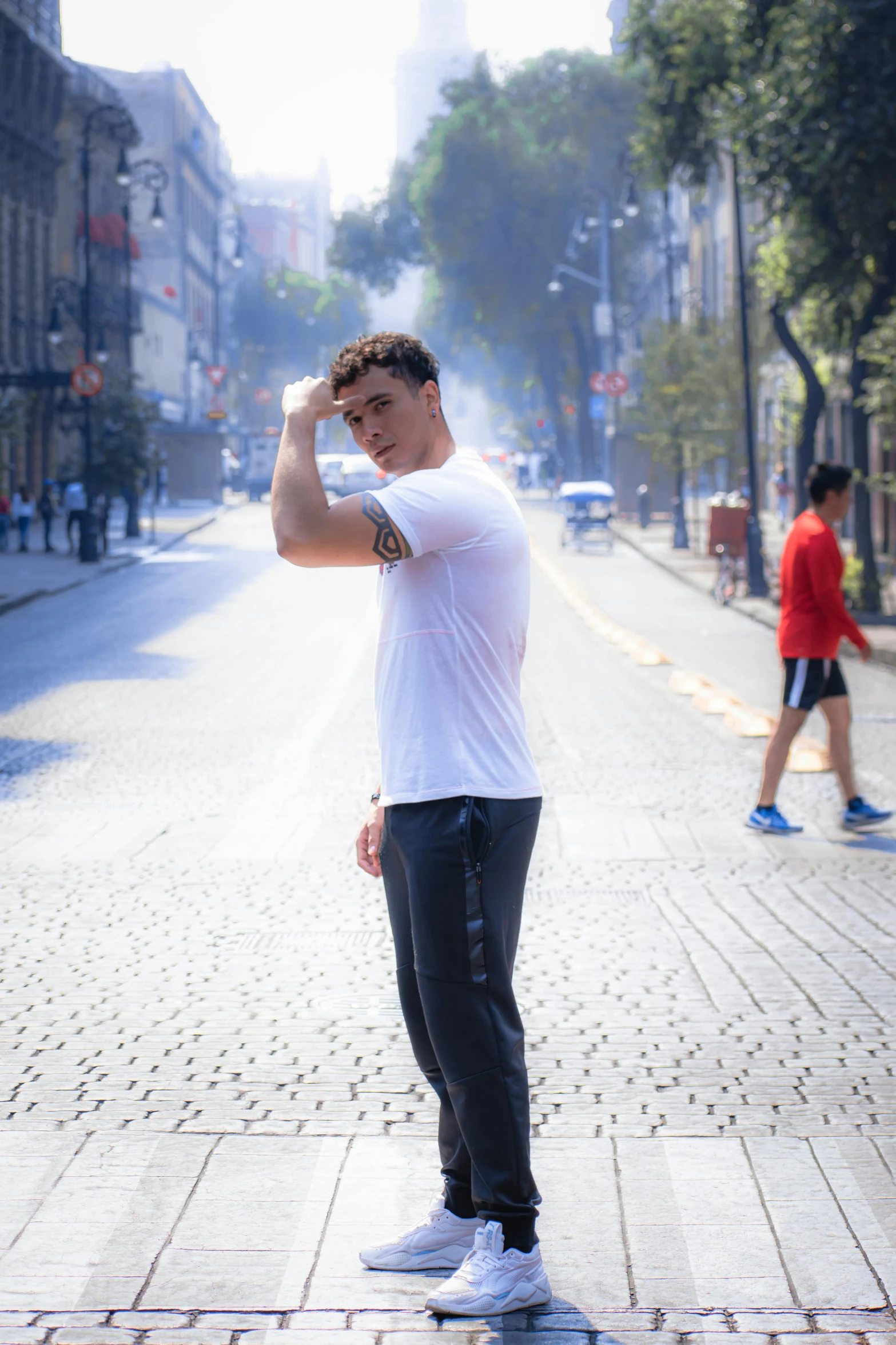 a young man wearing white stands alone on the street