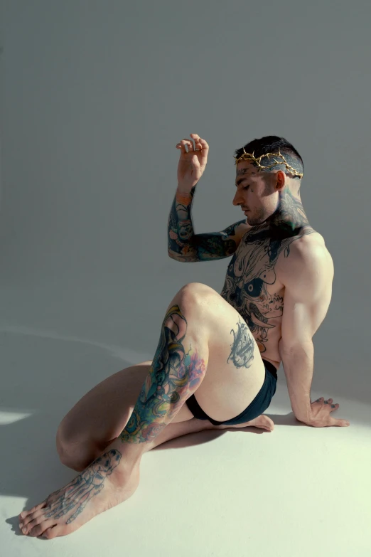 a tattooed man sitting on a white surface next to a glass of beer