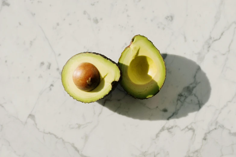 an avocado on a marble surface with half sliced