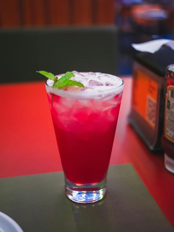 red cocktail with mint garnish on table in restaurant