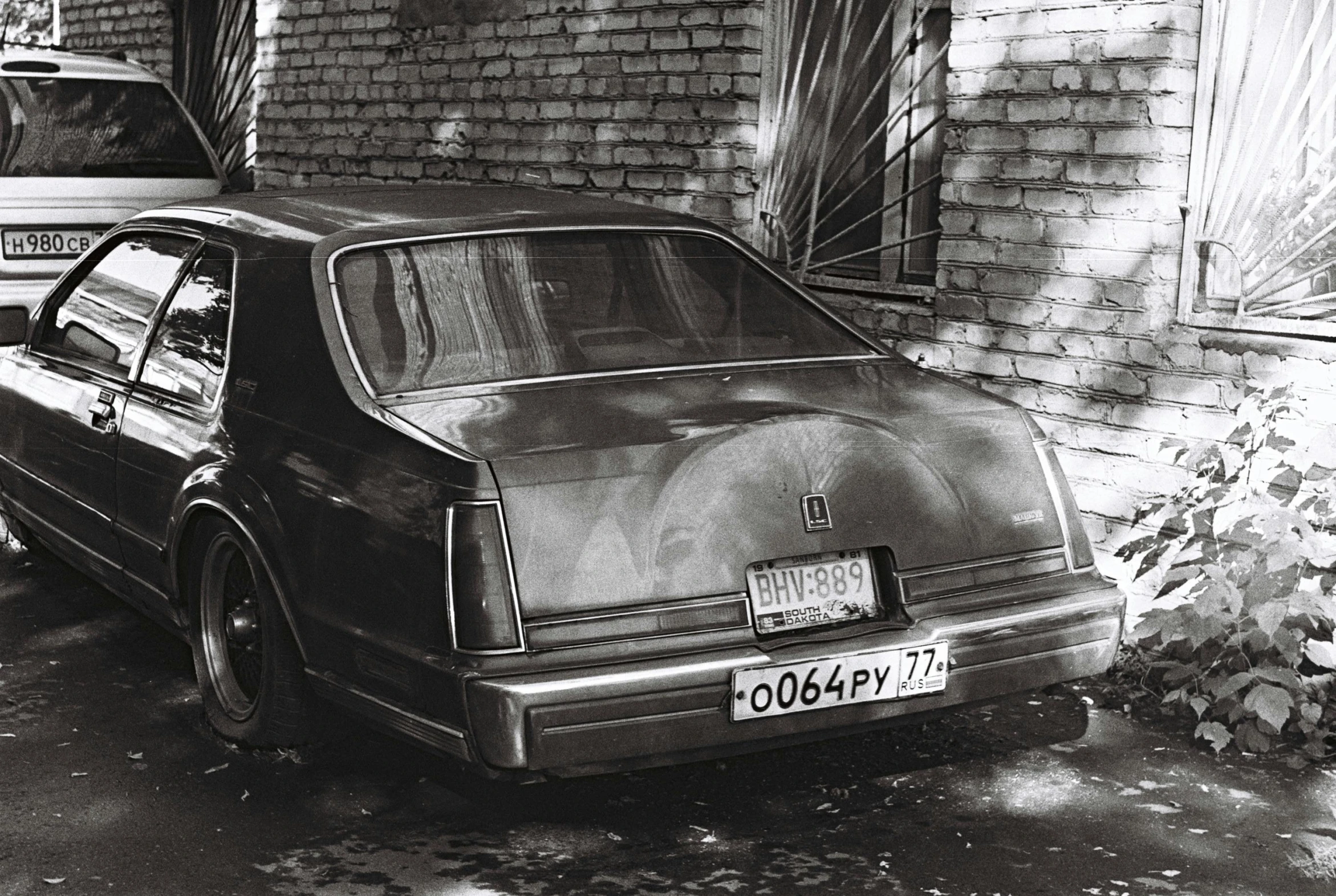 a black and white po of an old car parked on the side of a house