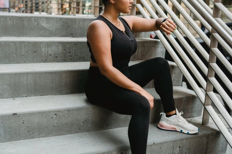 an african american woman sitting on steps in a black sports  top and leggings