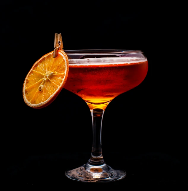 a glass with some sort of liquid next to a slice of orange